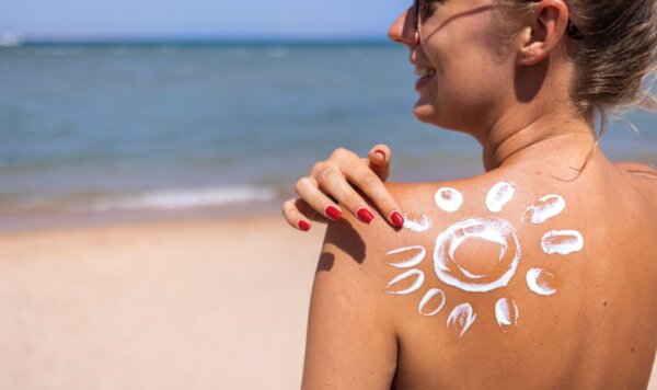 Γυναίκα έχει σχηματίσει έναν ήλιο με αντηλιακό στην πλάτη της. Κόνσεπτ χρήσης αντηλιακού βιοδιασπώμενου, για καθαρές θάλασσες και ωκεανούς.