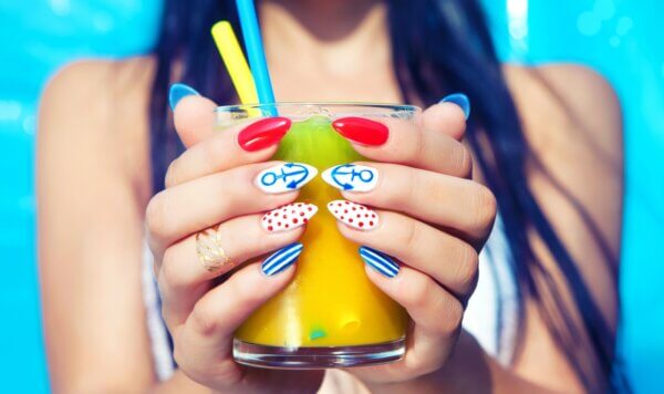 Νεαρή γυναίκα με καλοκαιρινά νύχια που έχουν σχέδια κρατάει ένα δροσιστικό ποτό.