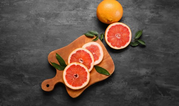 Κομμάτια γκρέιπφρουτ (grapefruit) που είναι τοποθετημένα σε έναν μαύρο πάγκο κι ένα ξύλο κοπής.